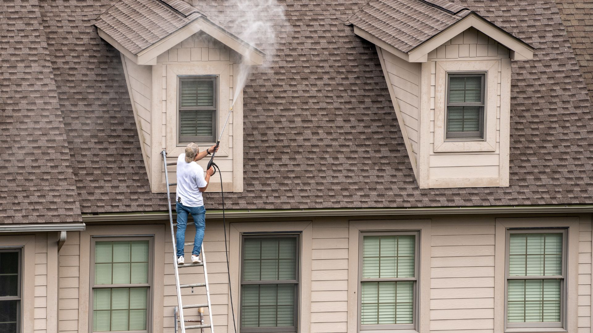 Person on ladder power washing house roof and exterior wall