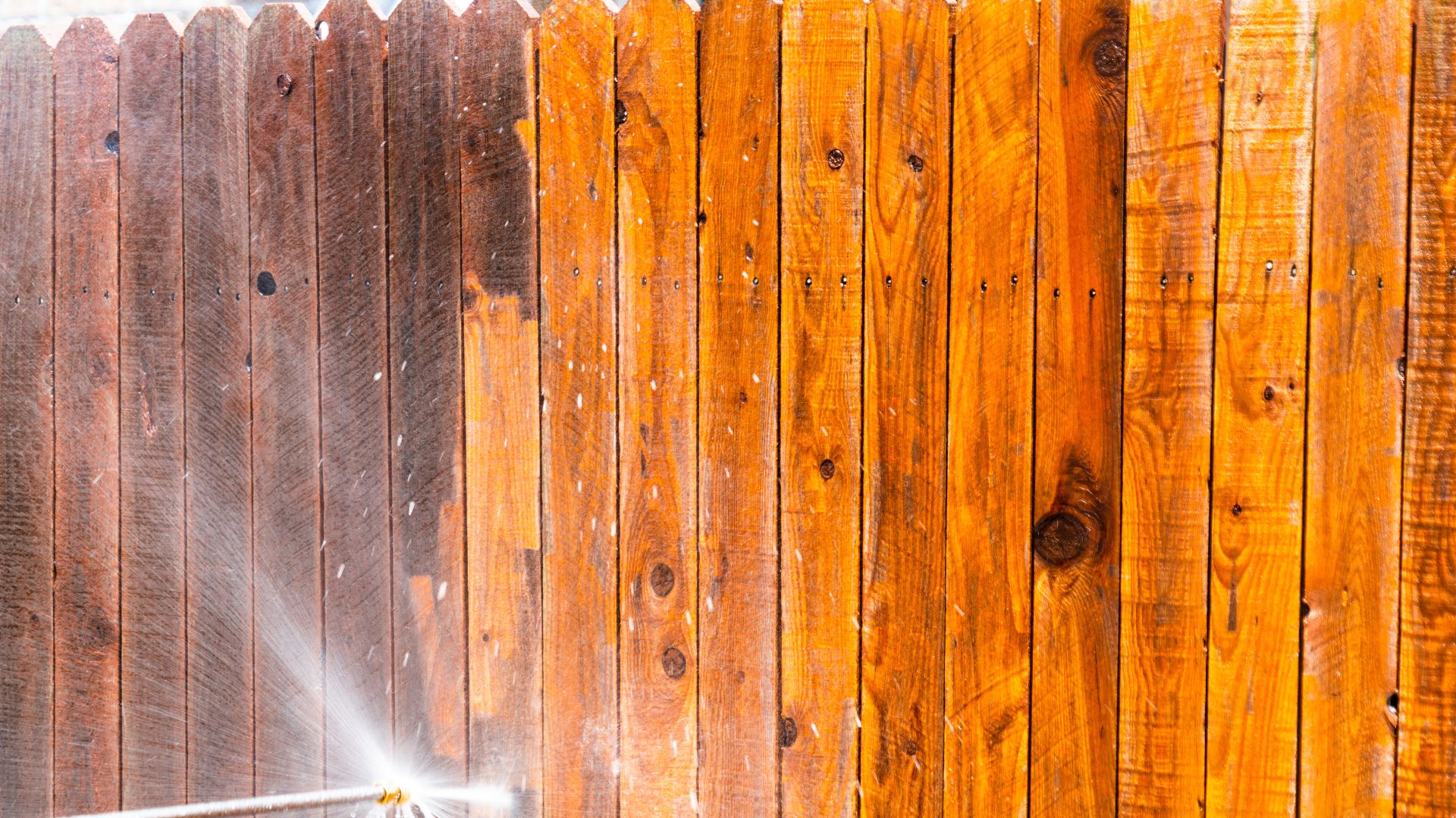 Wooden fence being pressure washed with water spray visible