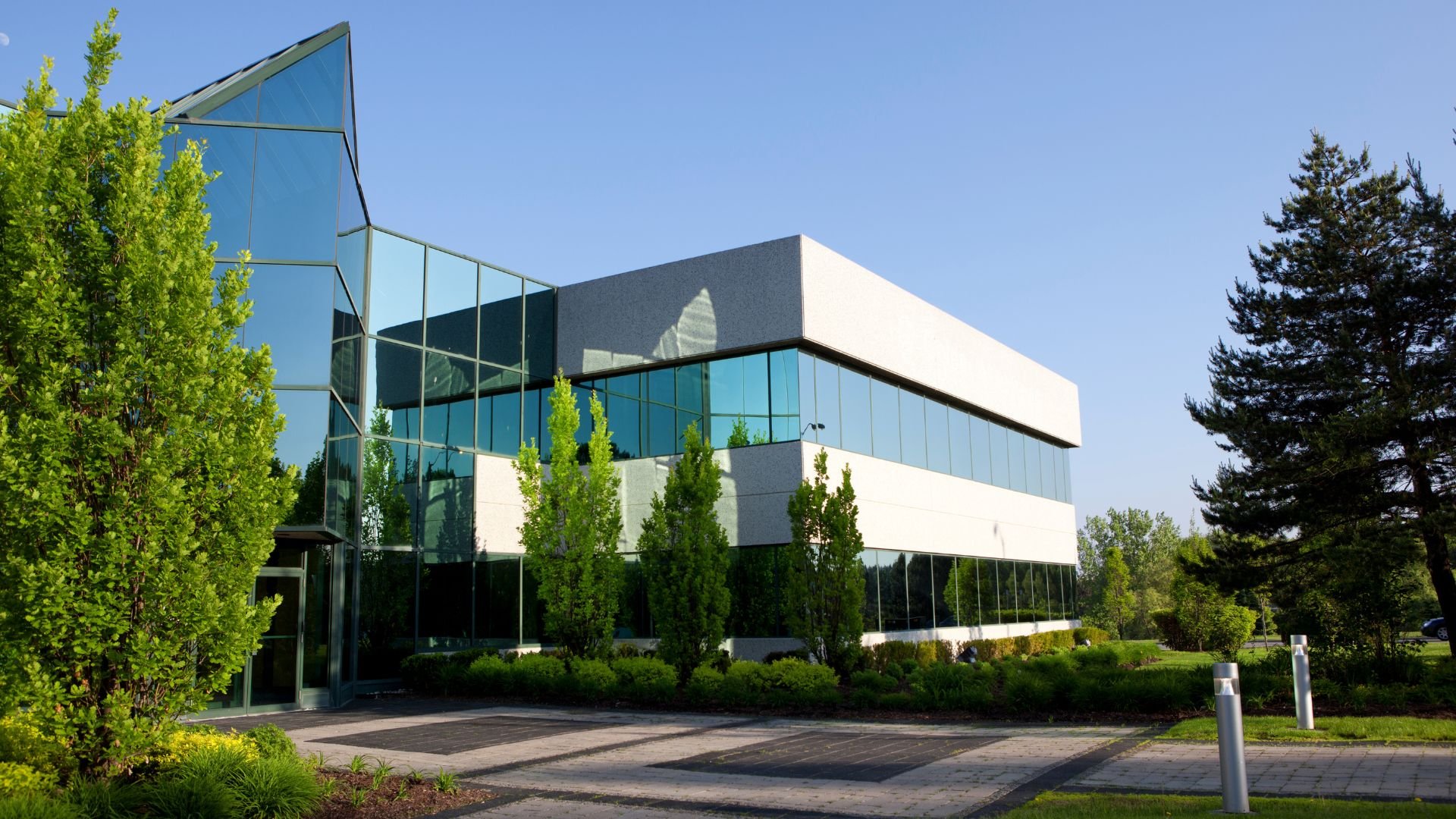 Modern glass and white office building surrounded by green trees