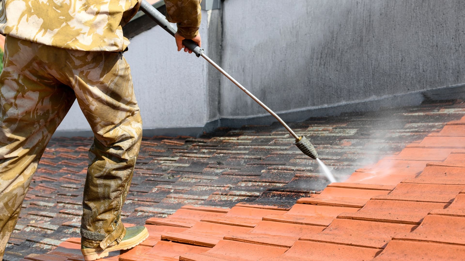 Person cleaning terracotta tiles with high-pressure water spray